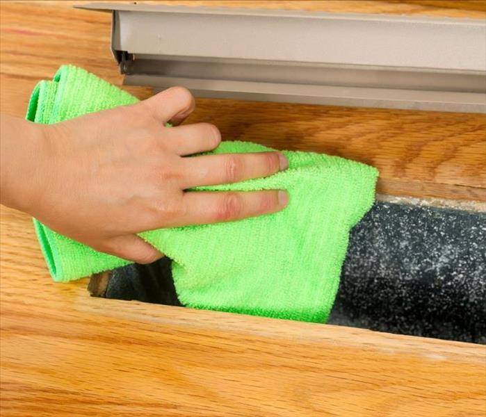 hand with green cloth cleaning floor vent